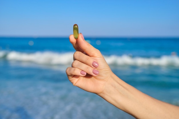 Vitamin D, capsule with fish oil in hand close-up, blue sky sea background. Health, nutritional supplements, vitamins concept