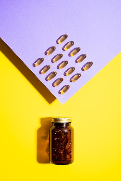 Vitamin d capsules omega pills in glass bottle on yellow lilac background with trendy shadows