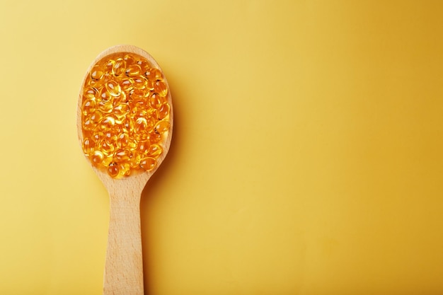 Vitamin D3 Capsules in a spoon with other vitamin D3 capsules around them on a yellow background