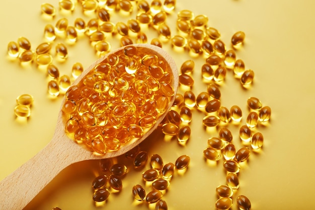 Vitamin D3 Capsules in a spoon with other vitamin D3 capsules around them on a yellow background