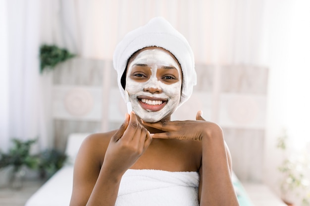 Maschera viso alla vitamina. donna sorridente africana con un viso in una maschera nella spa