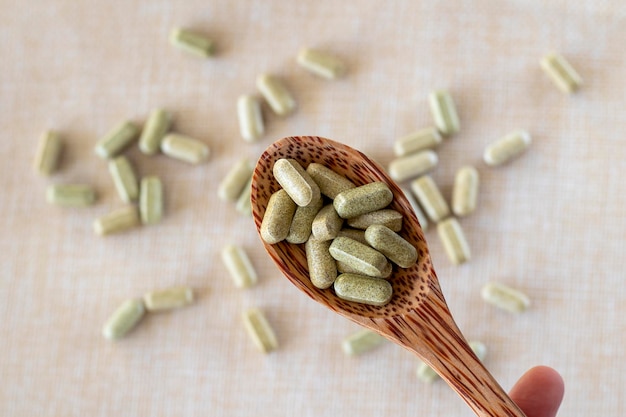 Vitamin from broccoli sulforaphane in capsules in a wooden spoon on a beige background Tablets and medicines in green