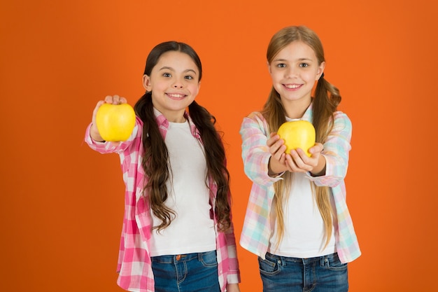 Vitamin fruit nutrition for children. Healthy lifestyle. Distributing free fresh fruit at school. Girls kids casual style eat apple fruit orange background. Schoolgirls eat apple fruit. School lunch.
