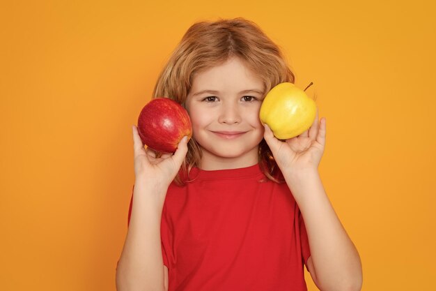 Vitamin and healthy fruits for kids Kid in red tshirt with apple in studio Studio portrait of cute child hold apple isolated on yellow background