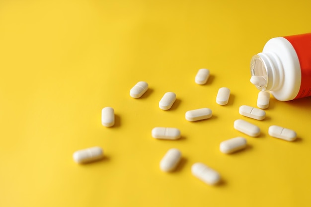 Vitamin or medication poured from a medical bottle on yellow background Creative flat lay