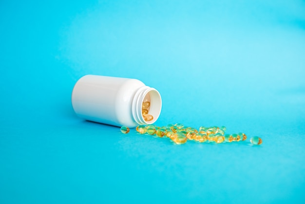 Vitamin medicinal capsules are poured from a white bottle on a blue background Covid 19 Health