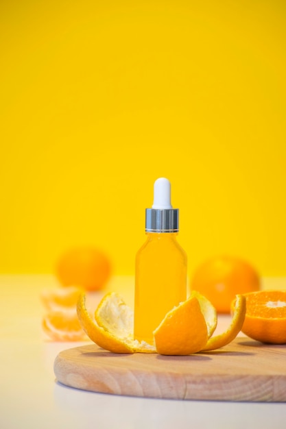 Vitamine C serum cosmetische fles in mandarijnschil met oranje stukjes op gele achtergrond met kopie ruimte.