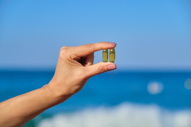 Vitamine D, capsule met visolie in de hand close-up, blauwe hemel zee achtergrond. Gezondheid, voedingssupplementen, vitamineconcept