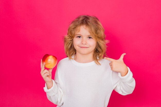 Vitamine en gezond fruit voor kinderen Jong geitje met appel in studio Studioportret van schattig kind houdt appel geïsoleerd op rode achtergrond