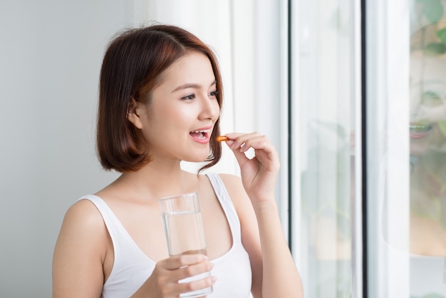 Vitamine En Supplement. Close-up van mooie jonge vrouw die gele visoliepil neemt.