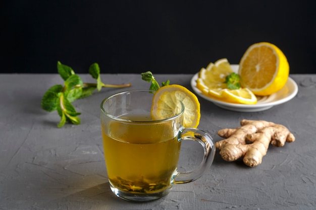 Vitamine gemberdrank met honingmunt en citroen in een glazen beker in de buurt van de ingrediënten op een betonnen achtergrond