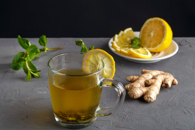 Vitamine gemberdrank met honingmunt en citroen in een glazen beker in de buurt van de ingrediënten op een betonnen muur.