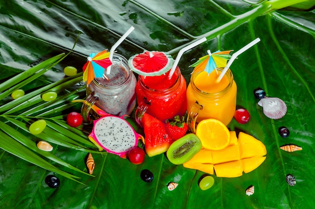 Foto vitaminen smoothie met watermeloen, mango en dragonfruit staande op het tropische groene blad. zomervakantie en verse maaltijd
