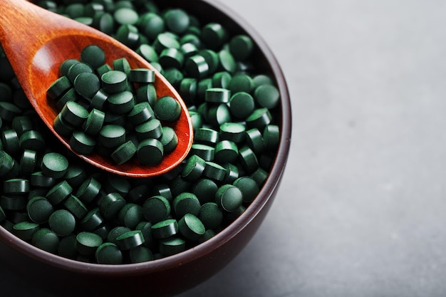 Vitaminen van spirulina in een houten beker met een houten lepel op een donkere achtergrond Vegetarische bron van aminozuren en omega 3