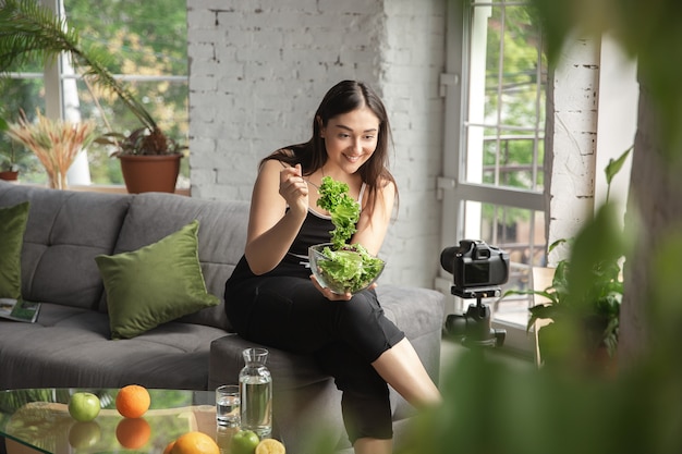 Vitamins. Caucasian blogger, woman make vlog how to diet and lost weight, be body positive, healthy eating. Using camera recording her green salad preparing. Lifestyle influencer, wellness concept.