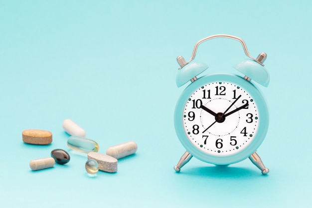 vitamins, supplements and alarm clock on pastel blue background. 