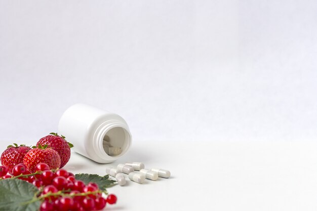 Vitamins supplements as a capsule with fresh berries from medicine white pill bottle.