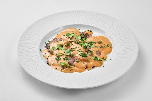 Vitello tonnato from veal with sauce in a white plate on a white background Closeup selective focus