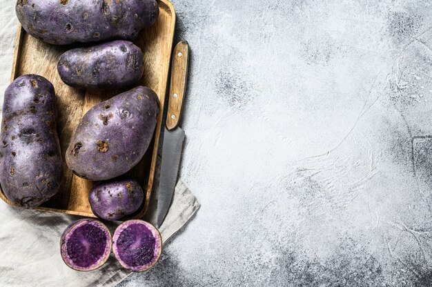 Vitelotte raw potato on a chopping Board. Gray background. Top view. Space for text