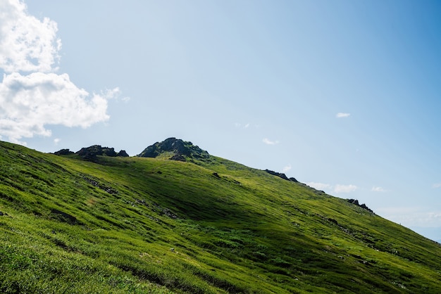 Ярко-зеленый холм с камнем на вершине под голубым небом с облаками.