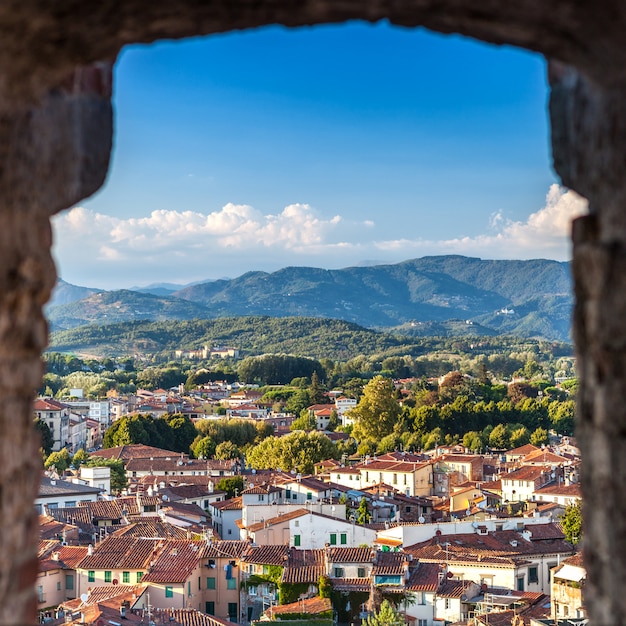 Vivid rooftops of city Lucca with background of colorful green mountains range, Italy.