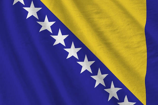 Vlag van Bosnië en Herzegovina met grote plooien die van dichtbij zwaaien onder het studiolicht binnenshuis De officiële symbolen en kleuren in banner