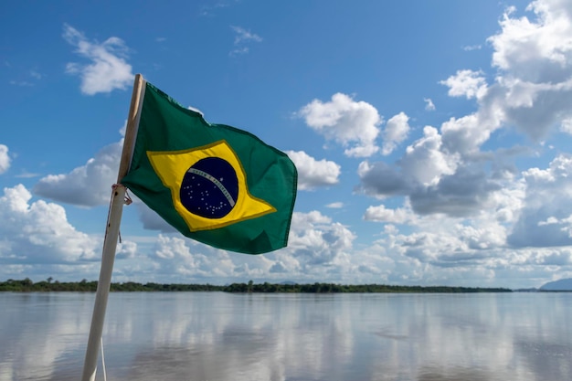 Vlag van Brazilië wapperend in de wind met rivierlandschap op de achtergrond