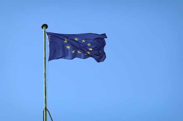 Vlag van de Europese Unie die op vlaggenmast op zonnige dag over duidelijke wolkenloze blauwe hemel golven