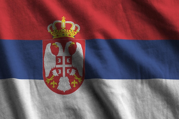 Vlag van Servië met grote vouwen die van dichtbij onder het studiolicht zwaaien De officiële symbolen en kleuren in banner