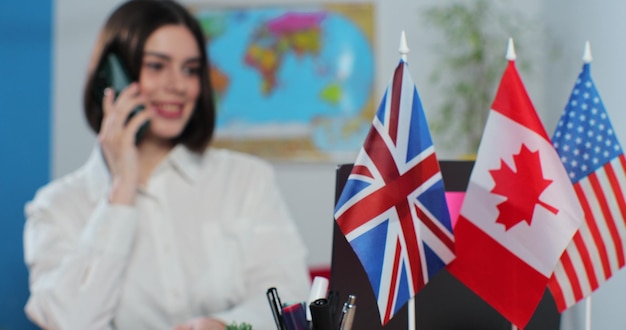 Vlaggen van verschillende landen op een tafel in een reisbureau op de achtergrond is een reisbureau vrouw aan de telefoon met een klant