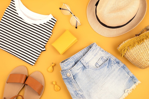 Vlakke leggen met vrouw modeaccessoires, jeans broek, hoed, zonnebril over gele muur. Mode, online beautyblog, zomerstijl, winkelen en trendsconcept. Bovenaanzicht