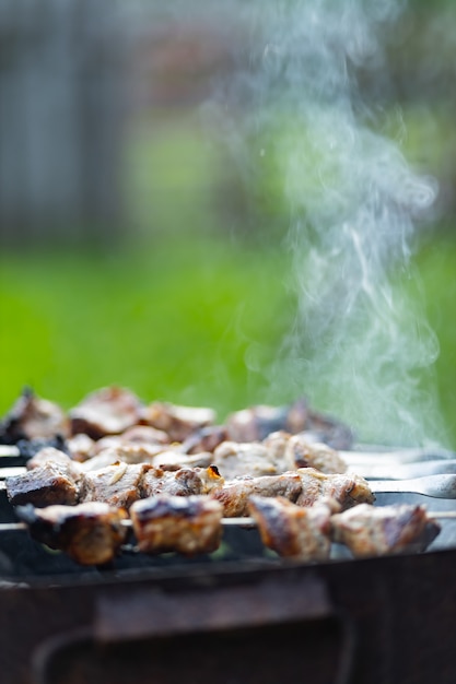 Vlees wordt gebakken op spiesjes op de mangal. Barbecue vlees op spiesjes in rook. Gegrilde kebab koken in een landhuis. Ruimte kopiëren