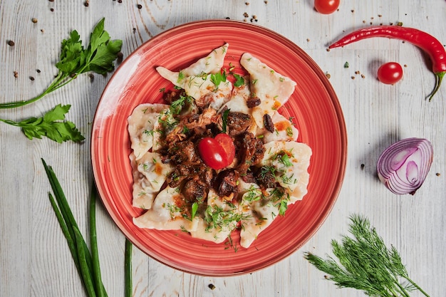 Vleesknoedels Russische pelmeni-ravioli met vlees op een witte plaat op een houten serveerplank