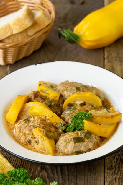 Vleeskoteletten met courgette in tomatensaus op een houten tafel.