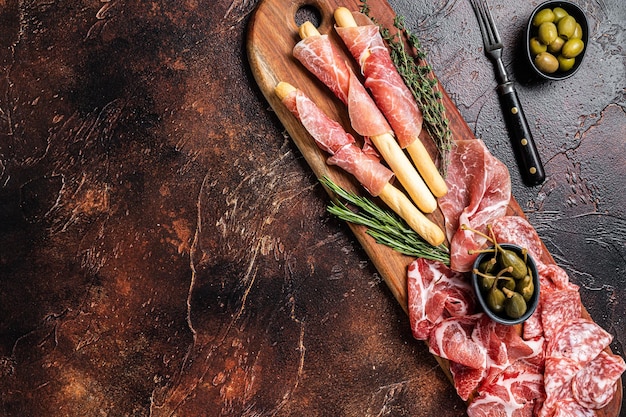 Vleesvoorgerechtschotel met grissini-sticks Prosciutto crudo Salami en Coppa Worst en olijven Donkere achtergrond Bovenaanzicht Kopieer ruimte