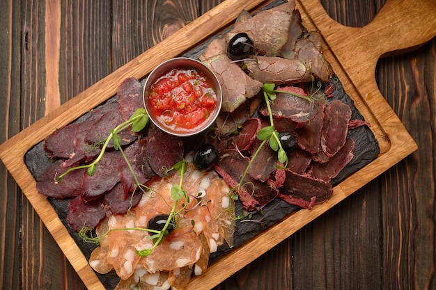 Vleeswaren, worst, basturma, gerookt vlees, met saus en olijven, op een houten bord, op een houten tafel