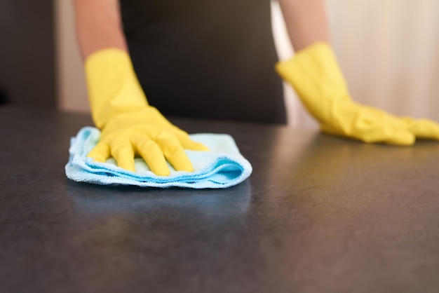 Vlekkeloos en kiemvrij Bijgesneden opname van een persoon die rubberen handschoenen draagt terwijl hij thuis een keukentafel afveegt met een doek