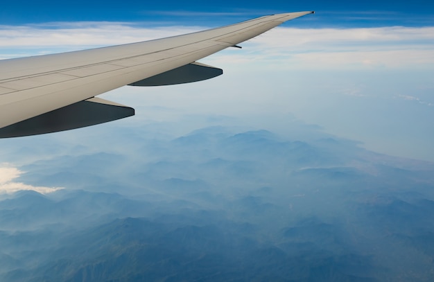 Vleugel van het vliegtuig over berg. Vliegtuig dat op blauwe hemel en witte wolken vliegt. Schilderachtig uitzicht vanuit vliegtuig raam. Commerciële luchtvaartmaatschappij vlucht. Vliegtuigvleugel.