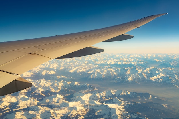 Vleugel van vliegtuig over bergdek met witte sneeuw. Vliegtuig dat op blauwe hemel vliegt. Schilderachtig uitzicht vanuit vliegtuig raam. Commerciële luchtvaartmaatschappij vlucht. Vliegtuigvleugel. Vlucht mechanica concept.