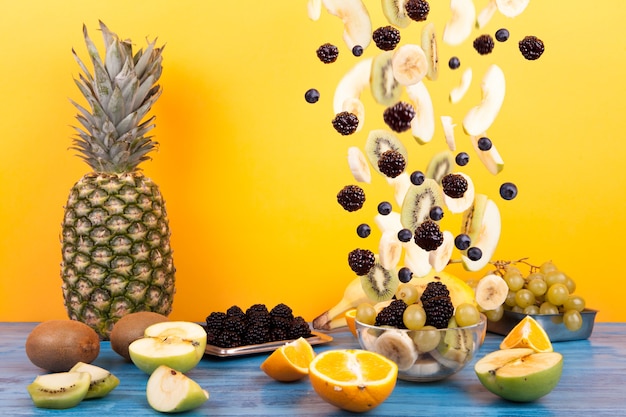 Vliegende gesneden fruit in glazen kom met fruitsalade op een gele achtergrond. Samenstelling van gezonde voeding