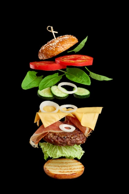 Vliegende hamburger ingrediënten: kotelet, sesambroodje, tomaat, ui, groene sla, kaas op zwart