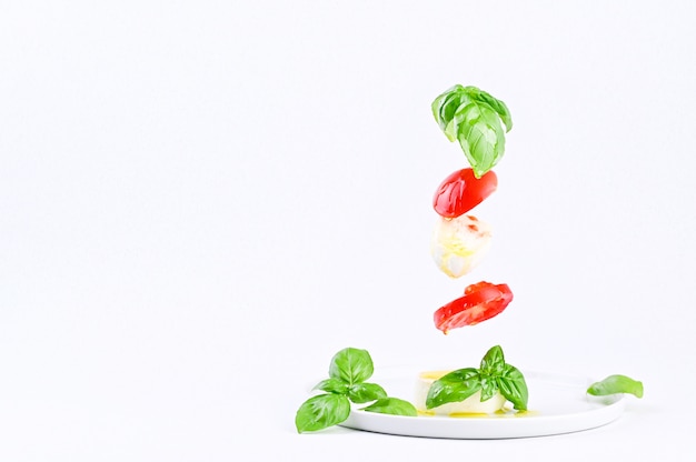 Vliegende salade in het frame. Traditionele Italiaanse Caprese Salade. Tomaten, mozzarella, basilicum, olijfolie