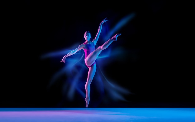 Vliegende vogel. Jonge en sierlijke balletdanser op zwarte studio achtergrond in neon gemengd licht. Kunst, beweging, actie, flexibiliteit, inspiratieconcept. Flexibele blanke balletdanser, gewichtloze sprongen.