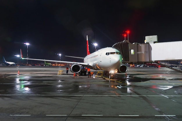 Vliegtuig bij passagiersgangpad van het terminalgebouw bij de luchthaven bij nacht, vliegtuigvluchtonderhoud.