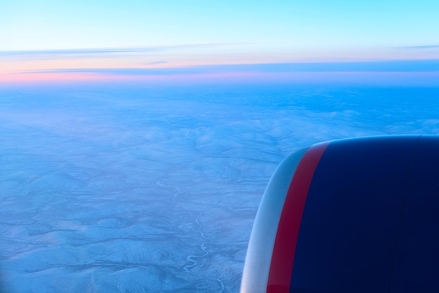 Vliegtuig dat op de blauwe lucht boven de bergen vliegt Een uitzicht op de prachtige zonsopgang vanuit het vliegtuigraam Vlieg- en reisconcept