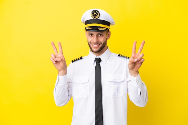 Vliegtuig kaukasische piloot geïsoleerd op gele achtergrond met overwinningsteken met beide handen