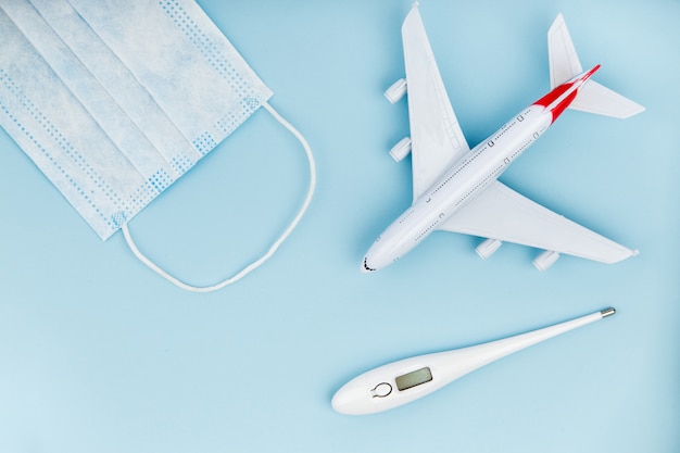 Foto vliegtuig, medische masker en thermometer op een blauwe achtergrond.