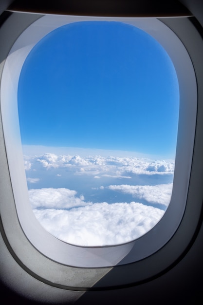 Vliegtuig patrijspoort raam met uitzicht op prachtige witte cumulus wolken en blauwe lucht