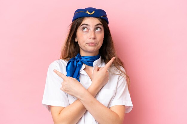 Vliegtuig stewardess blanke vrouw geïsoleerd op roze achtergrond wijzend naar de zijtakken die twijfels hebben