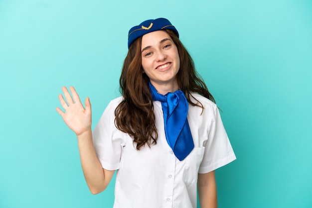 Vliegtuig stewardess vrouw geïsoleerd op blauwe achtergrond saluerend met de hand met gelukkige expressie